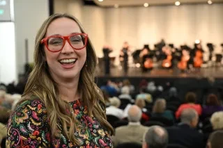 Woman smiling at camera with symphony on stage in background.