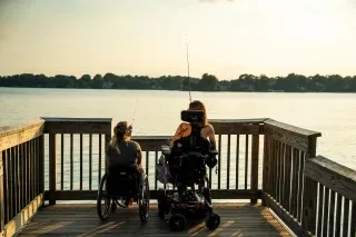 Two women, one using a motorized wheelchair and the other a manual wheelchair, fish from the ADA-compliant pier at Ramsey Creek Park, Lake Norman. 