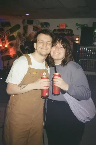 Couple smiling while holding red drink cans at bar.