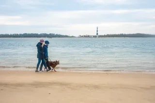Couple walking dog on Shackleford Banks in winter with Cape Lookout Lighthouse in distance across water.