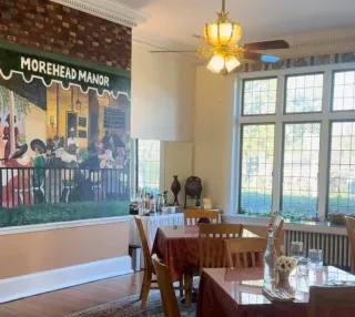 Dining room inside Morehead Manor in Durham with mural on wall.