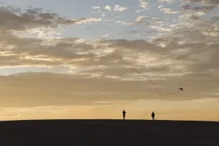 Man and woman fly a kite during a vibrant sunset at Jockey's Ridge State Park. 