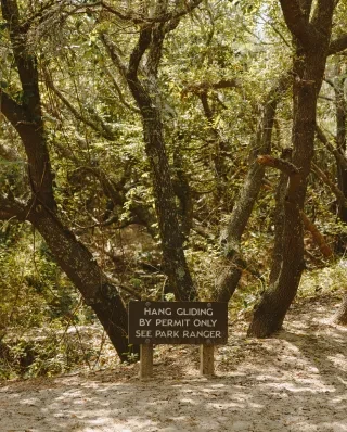 Hang gliding by permit sign at Jockey's Ridge State Park with rugged trees behind it.