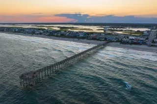 Aerial of Surf City Pier extending into water with land in background.