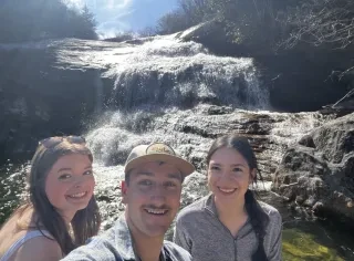 Two girls and a guy taking a selfie in front of a waterfall.