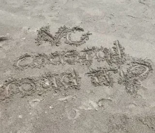 "NC Coastal Road Trip" written in sand in Oak Island.