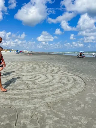 Man walking on sand maze in middle of beach.