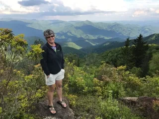 Woman standing on rock smiling at camera with beautiful mountains in background