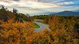 Aerial of curvy road climbing Grandfather Mountain during fall with mountains in distance.