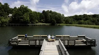 People fishing off large wooden fishing pier into Lake Coffey with trees in background.