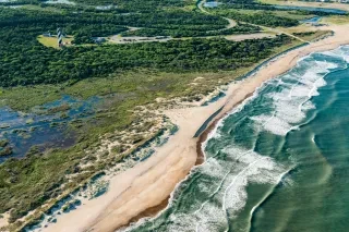 Aerial view of Atlantic coastline in summer with Cape Hatteras Lighthouse in upper left corner.