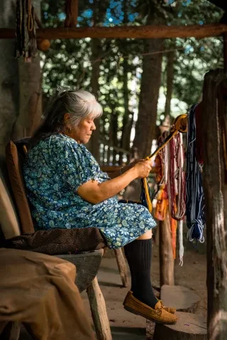 Older woman sitting and working on string crafts in Oconaluftee Indian Village 