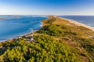 Aerial of Cape Lookout lighthouse and seashore surrounded by land and water.