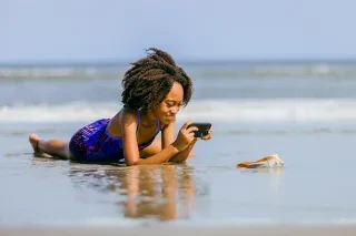 Girl taking picture of seashell on beach, leaving it as she's finding it.