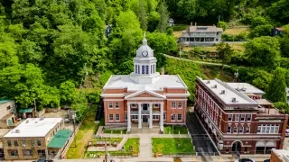 Madison County Courthouse featured in center of frame in Marshall with green trees and smaller buildings surrounding it.