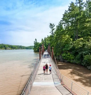 A family walks across a wooden bridge over a river along the Hickory Riverwalk.