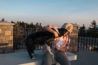 Woman's dog playfully licking her face on bench within Mt. Mitchell State Park.