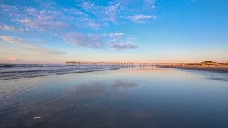 Pier in distance jutting into ocean with empty, serene beach in foreground.