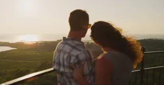Back of couple embracing on top of lighthouse and looking out over beautiful coastline.