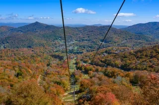 Aerial of chairlift ride in Sugar Mountain overlooking fall foliage in the mountains.