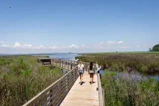Two friends walking on wood trail over sound and marshy waters in Corolla.