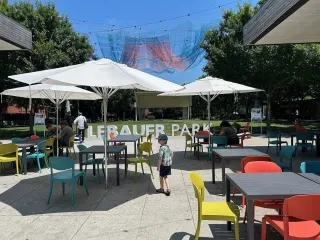 Boy walking through colorful tables and chairs in LeBauer Park under whimsical aerial art.