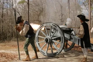 Men in period dress firing a cannon in a wooded area