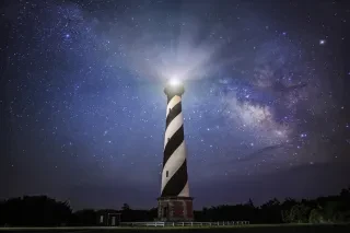 Lighthouse with a black and white diagonal daymark against a starry sky.