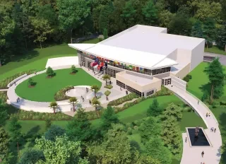 Rendering of a building with an angled roof and a smaller rectangular building attached. US, NC, US Navy and US Marine Corps flags fly above the entrance. Lawns and walkways surround the structure.