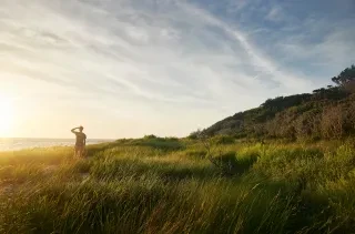 Wide landscape view of man looking out towards water at Springer's Point Reserve at Ocracoke Island during sunrise surrounded by dunes and grass.