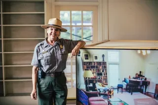 A smiling woman Park Ranger stands next to a display case at Carl Sandburg Home