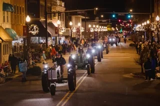 Parade of tractors riding through Elizabeth City Main Street at night.