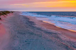 Calm, empty Hatteras Island beach with lazy waves rolling in under brilliant orange sky.