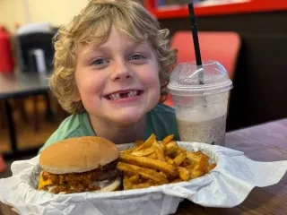 Child smiling for camera with plate of burger and fries in front of him.