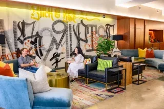 Two people conversing on hotel lobby couches with cool graffiti wall behind them.