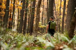 A hiker glances back while moving through a dense, colorful woodland, showcasing the serenity of the forest environment during the Outdoor NC Guide Summit at Forest Ridge State Park.