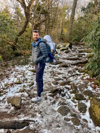 Man with daughter on back and dog behind him on way up Beacon Heights Trail during daytime.
