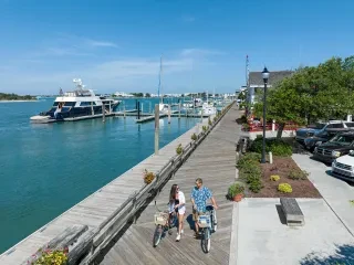 Couple walking their bikes on boardwalk in charming Beaufort with water to left during daytime.