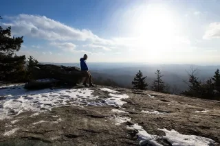 Person on top of wintry mountain trail with vista views in distance under bright winter sky.