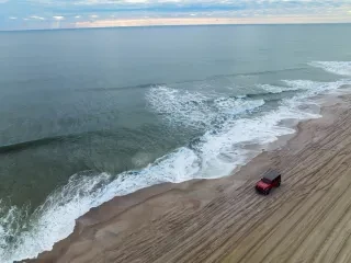 4x4 vehicle driving on sand alongside expansive ocean to the left on moody winter day in Kure Beach.
