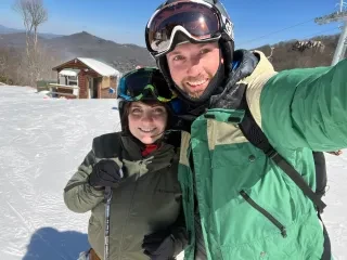 Couple posing for selfie wearing ski gear on snowy mountain during daytime.