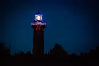 Top of Currituck Beach Lighthouse strung with holiday lights at night.