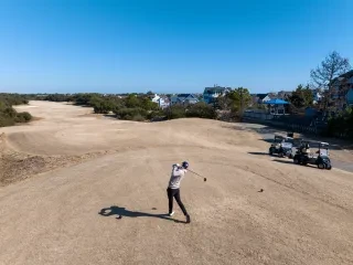 Person teeing off on golf course in Corolla during winter.