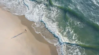 Aerial of person surf casting on sand into ocean on beautiful day.