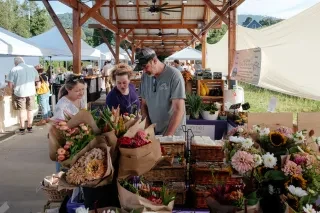 People looking at hand-picked flowers at Yancey County Farmers Market with more vendors in background.