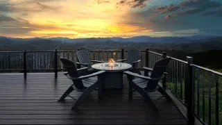 Adirondack chairs sitting around a fire pit on patio with beautiful sunset over mountains in distance.