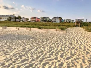 Beach houses in a line in background with soft sand in foreground.