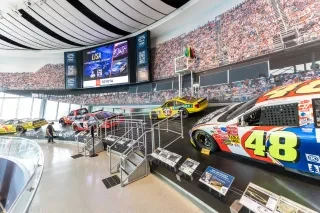 Museum exhibit of race cars and race trucks throughout the history of NASCAR, placed on a banking imitating a race track.