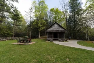 House and wagon on display surrounded by green trees and foliage during daytime.