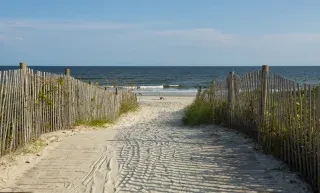 Beach access heading down to beach where person is seated on beach chair.